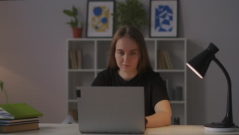 Una-Joven-Encantadora-Está-Usando-Internet-Con-Una-Computadora-Portátil-Por-La-Noche-Descansando-En-Casa-Y-Navegando-Por-Las-Redes-Sociales-Sentada-En-La-Mesa-En-El-Salón-Retrato-Medio